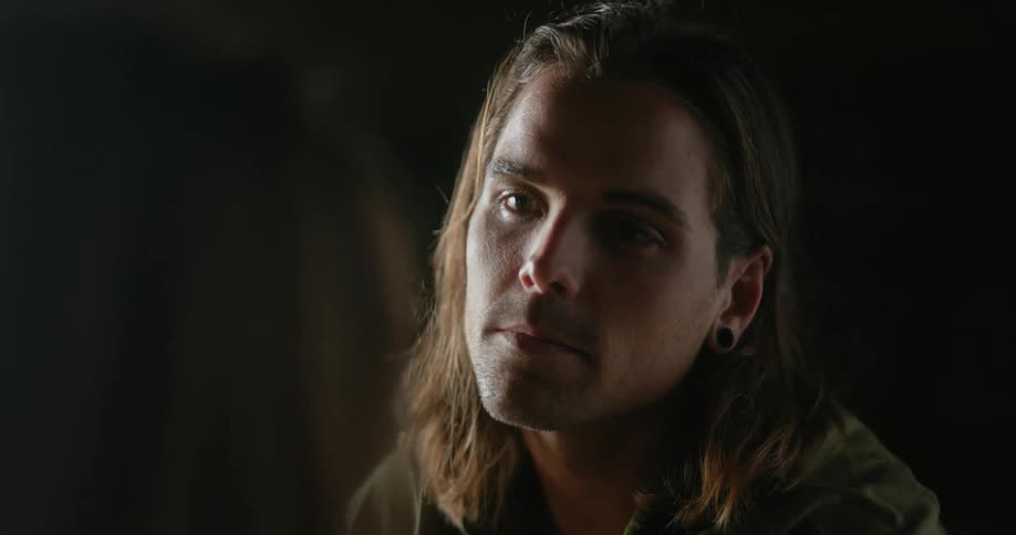 Young long haired man lovingly looking at his couple inside a dark room