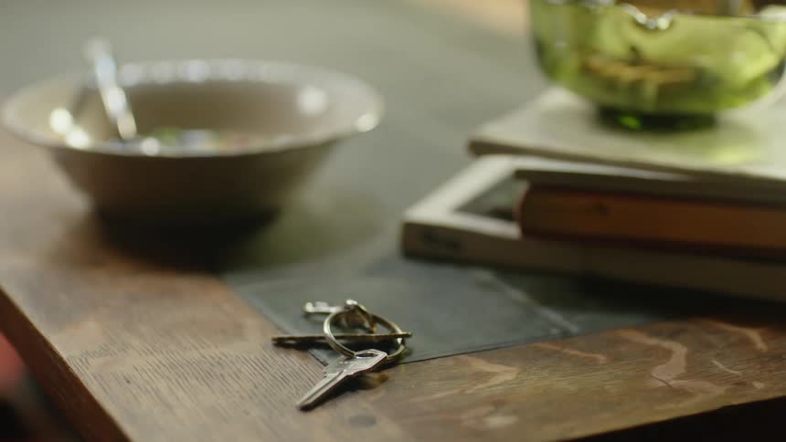 Person picks up keys sitting on coffee table near books and a couple of bowls