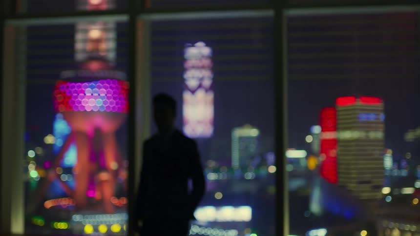 A silhouette of a man in a highrise building looking at the city skyline out of the window