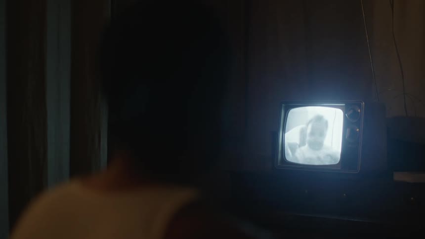 A person sits in a darkened room watching a home movie on a small television