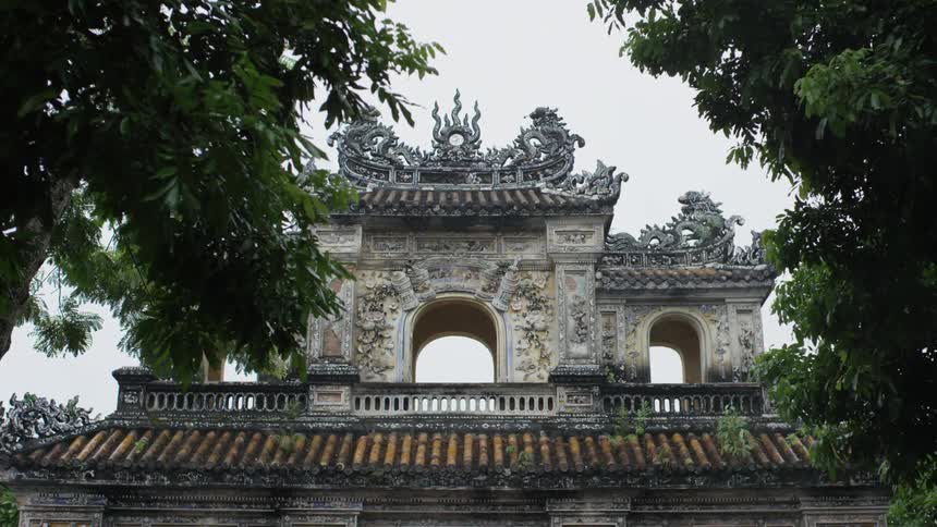 Sculptured dragons sit on roof of ornate detailed and painted structure under clear pale blue sky