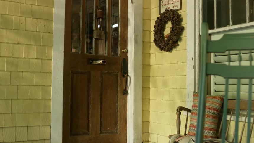 A thrown newspaper hits the door of a house and falls onto a stack of newspapers on the porch