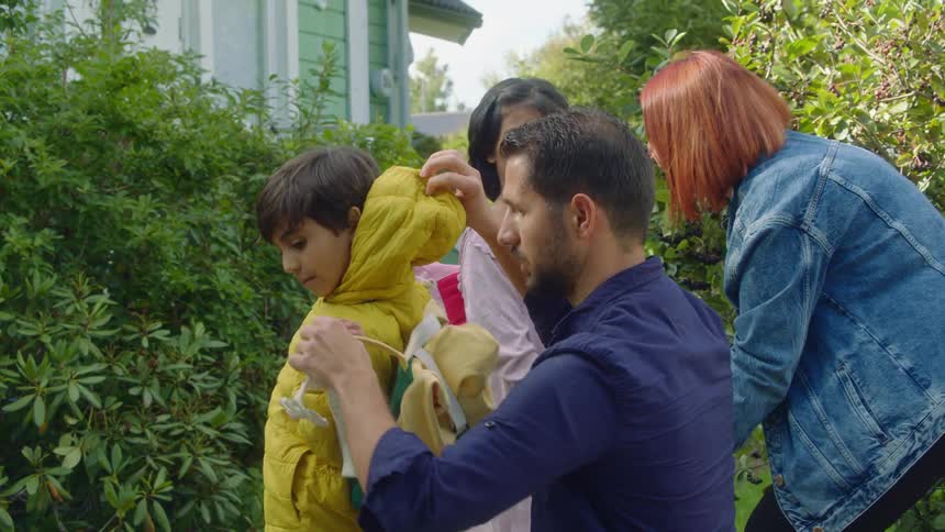 A man a woman a boy and a girl in front of a house surrounded by bushes with the sky and clouds in the background