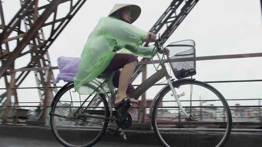 A woman rides her bicycle across a large bridge on a rainy and overcast day