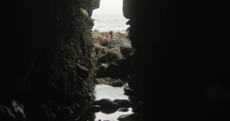 View through the opening of a cave of a couple sitting on the rocks spending time together