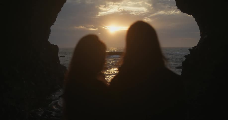 Silhouette of a young couple looking at the sunset over the ocean from a cave in the coast