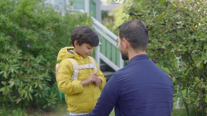 A man gives his son a pep talk outside their house before sending the boy off to school