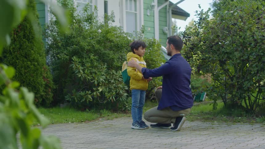 A man talking to a boy with a jacket and backpack in front of a house