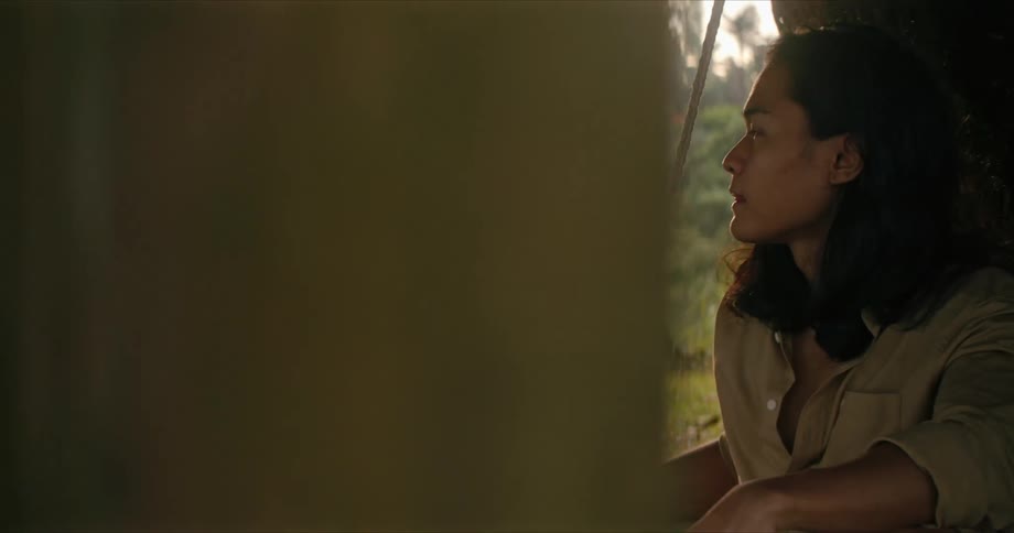A young woman swings in a round swing outside by a lake with a young man sitting beside her