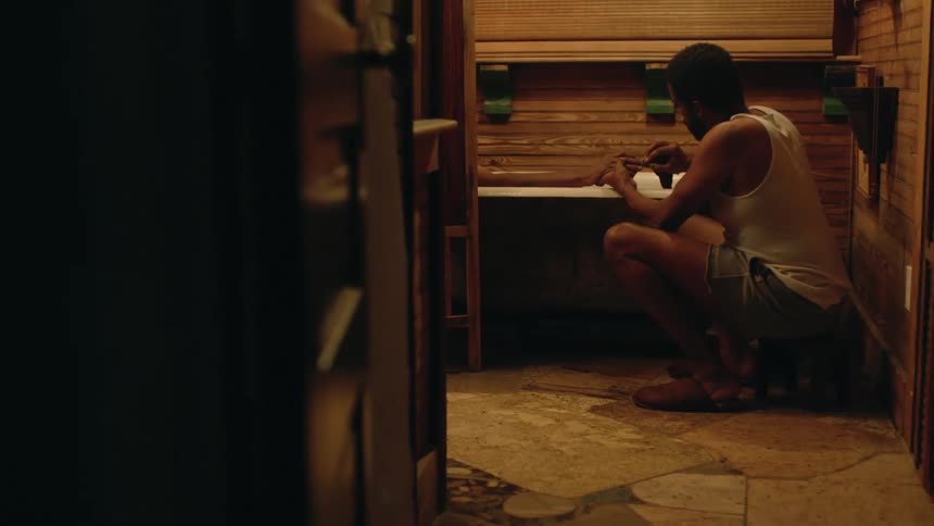A man kneeling beside a bathtub uses a washcloth to clean the nails of another person sitting in the bathtub