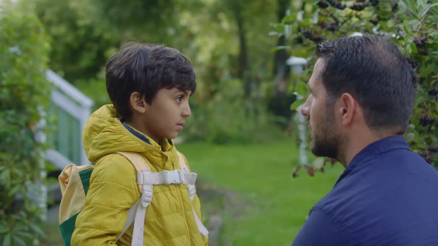 A man talking to a boy with a jacket and backpack in front of a house