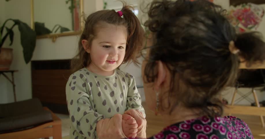 A woman holds and moves a young girls hands as they play a game together