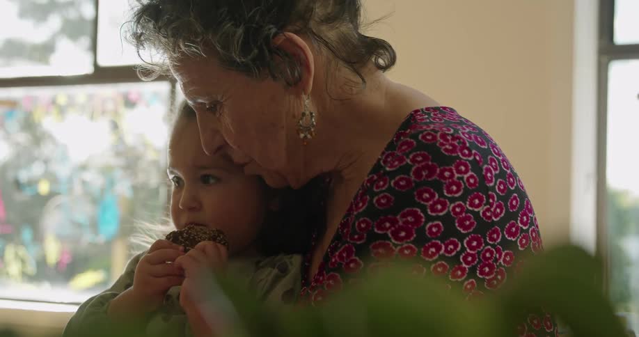 Grandmother holds and rocks granddaughter as the girl nibbles