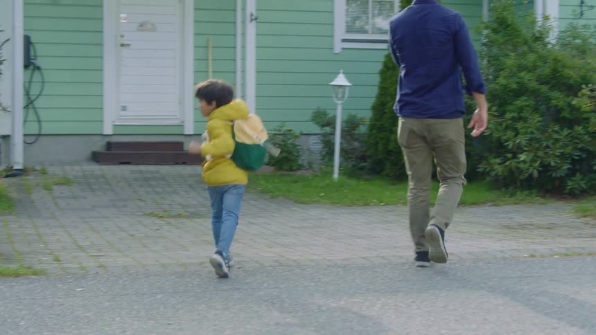 Boy wearing backpack run past house to greet his father near their home