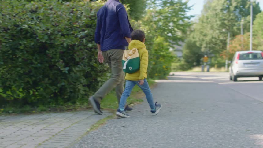 Father kneels to talk to son wearing jacket and backpack then takes his hand and walks him out to and down the street as car drives through neighborhood