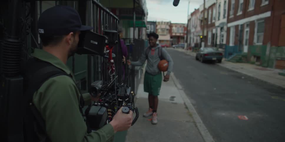 A man carrying a basketball is being filmed on a street