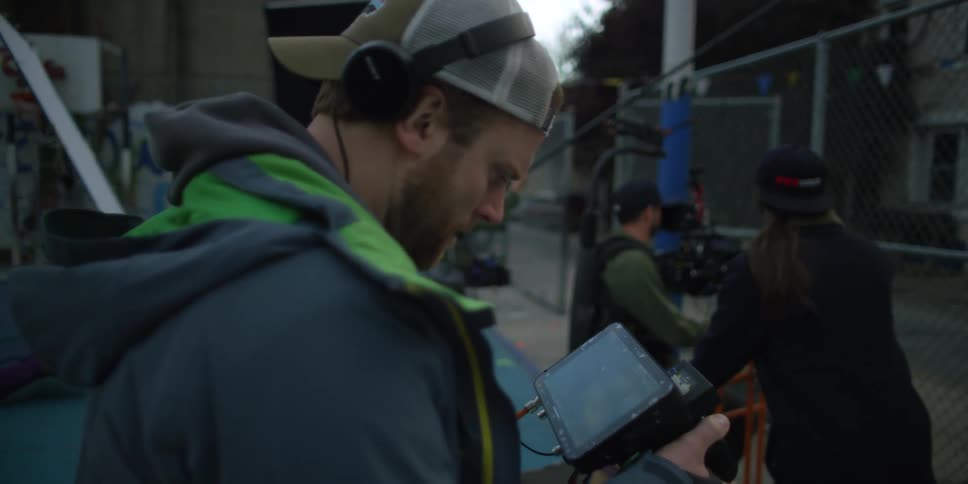 News reporter stands outside looking at his camera