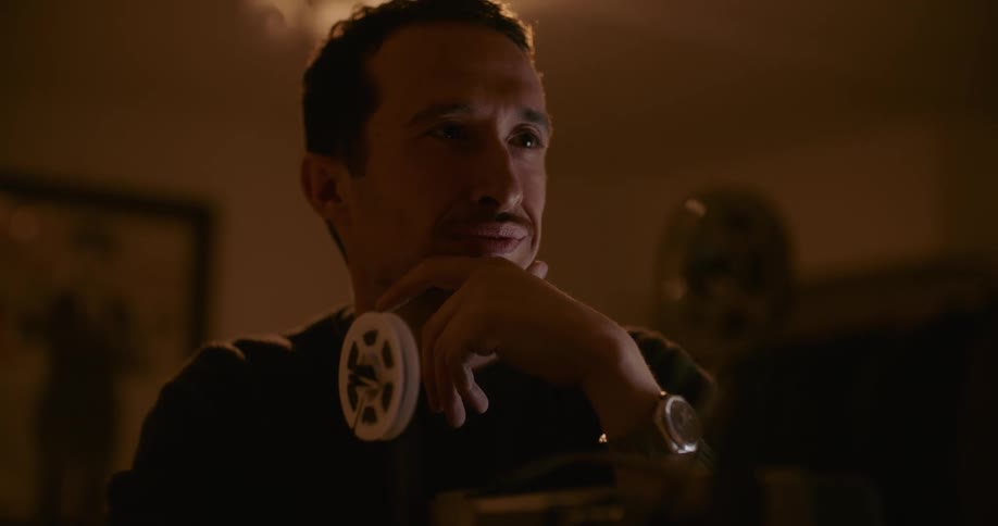 Man holding his chin watches through old movie projector with reels