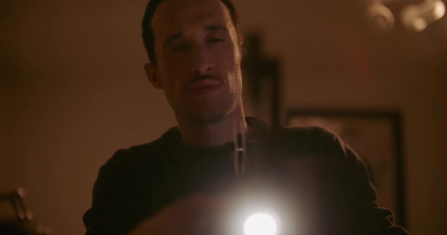 A man in a room adjusting a projector with a wall and a picture frame in the background