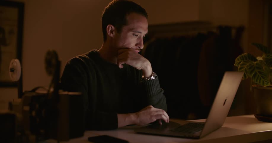 A man uses his laptop in a dimly lit room at night