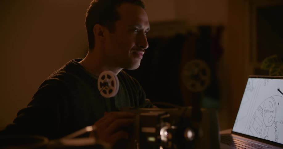 Man studies illustration on laptop screen smiling as he is able to work film projector