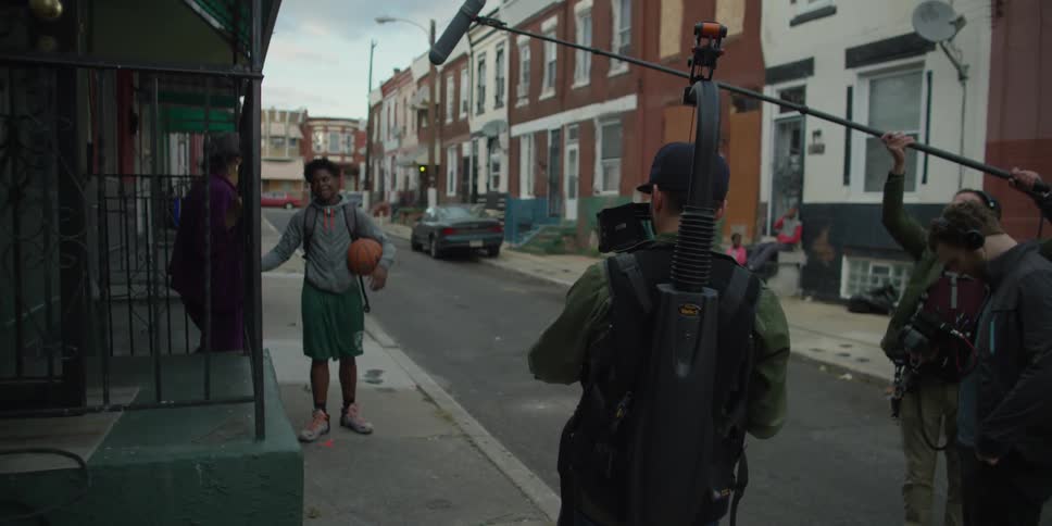 A film crew is filming two people talking on the sidewalk