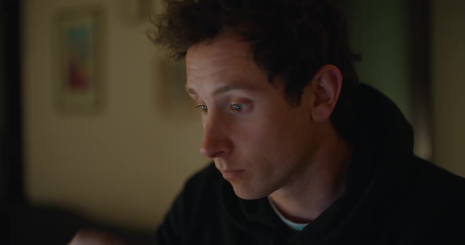 Man sits in dim room typing on keyboard briefly rubbing his face