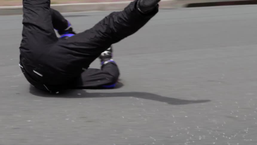 A person with a helmet and gloves sliding down a road with a pavement and plants in the background