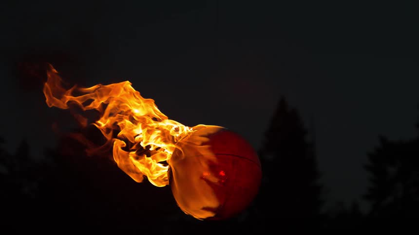 A ball on fire with trees the sky and clouds in the background