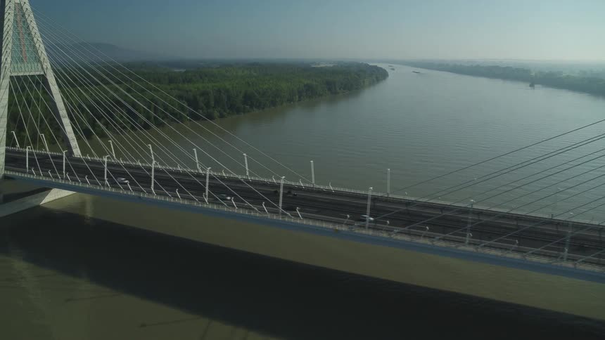 Traffic crosses river on suspension bridge with mist covered forest mountains and lake in background