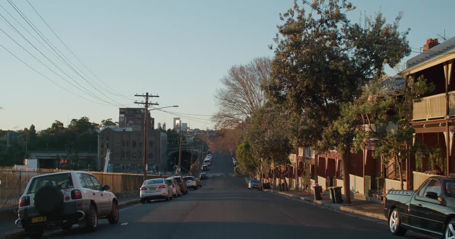 A city street with vehicles trees and buildings with the sky and clouds in the background