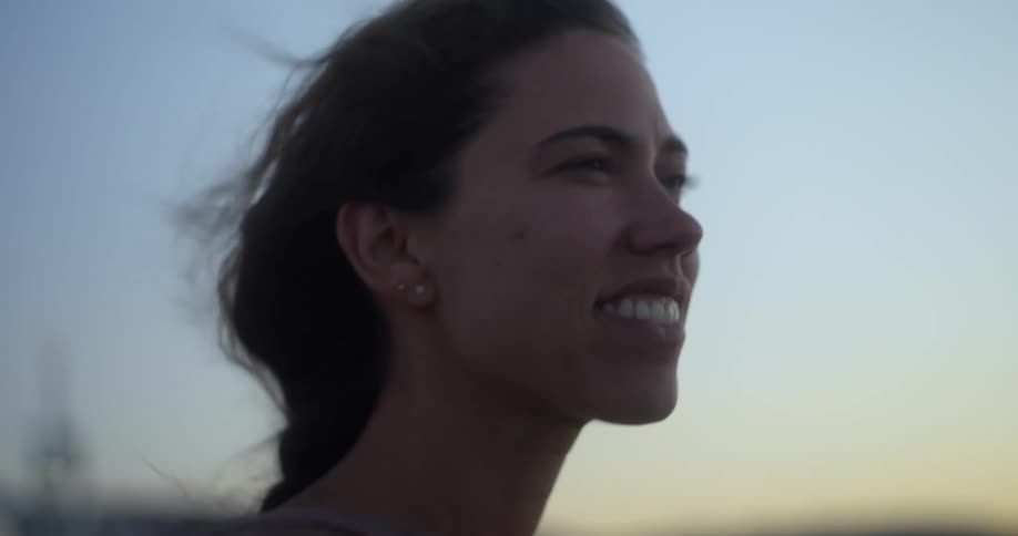 A young woman smiles as she stands outside with the wind blowing in her hair