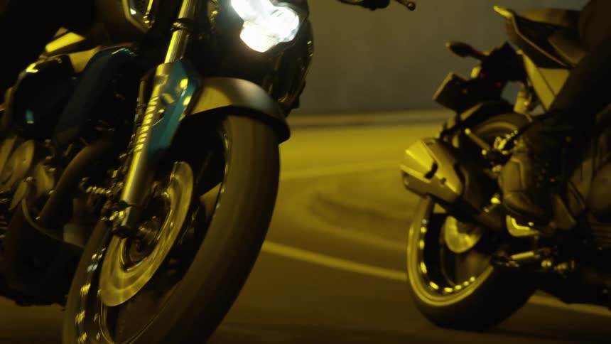 Two motorcycles ride side by side through a city tunnel