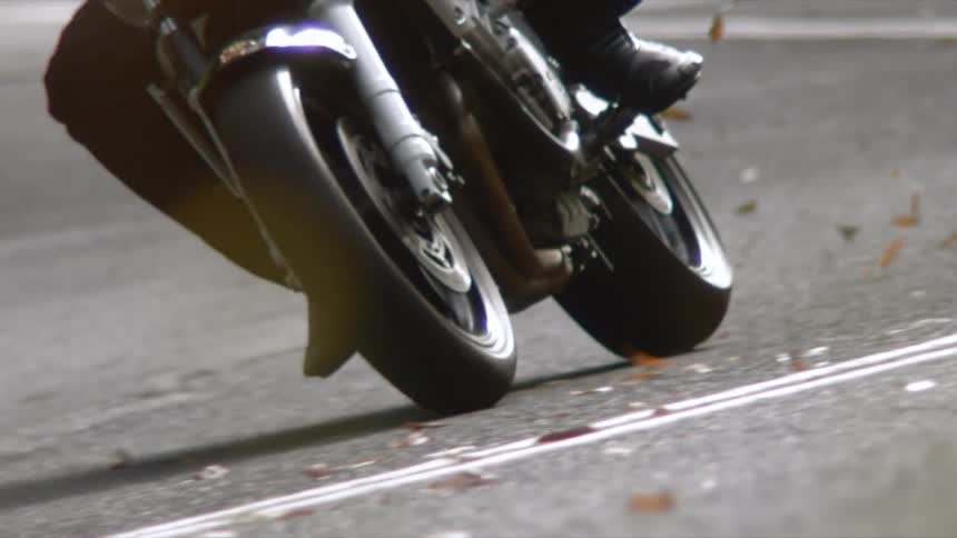 A person riding a motorcycle on a road with leaves with a guardrail and grass in the background