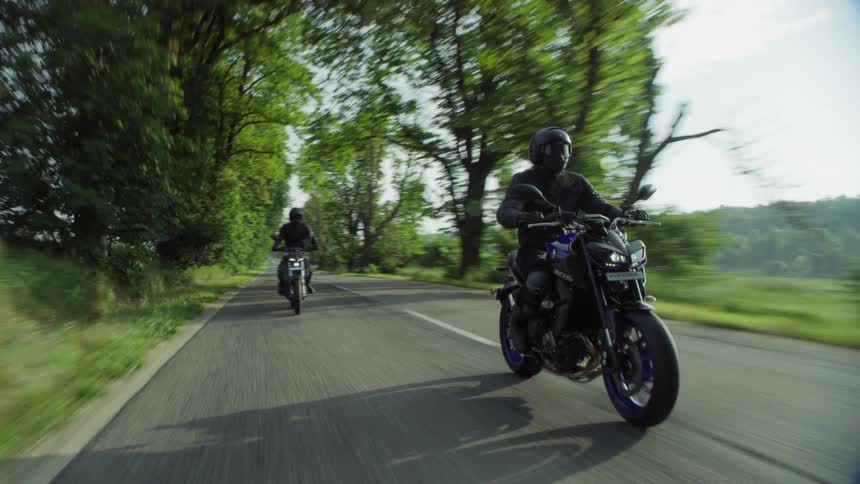 Two people ride motorcycles on a rural roadway