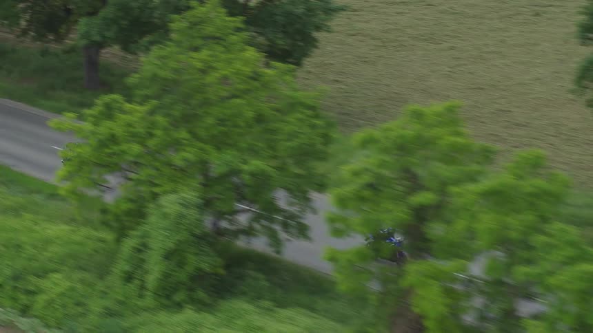 Three people drive motorcycles down a street next to a grassy field