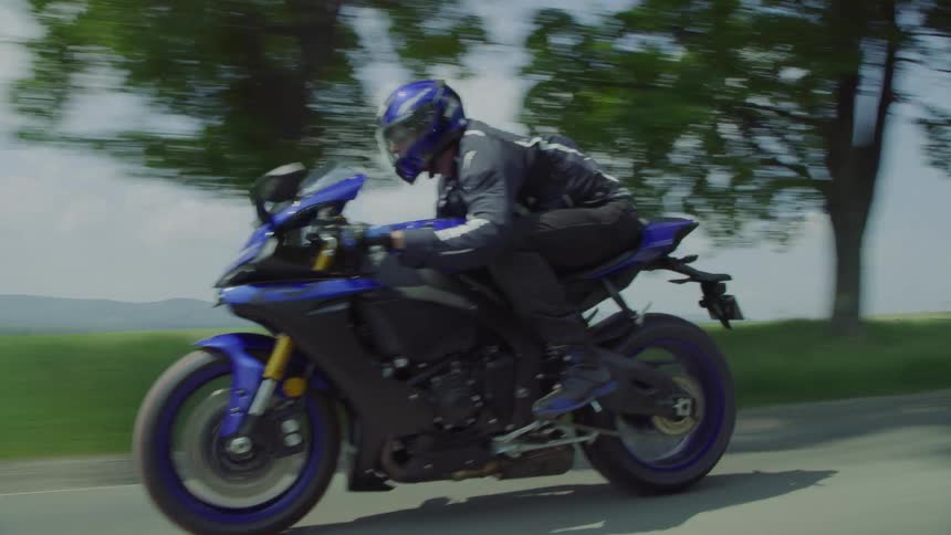A motorcyclist speeds down a road in the countryside on a bright day