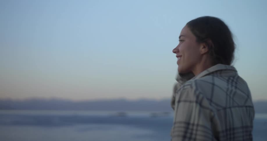 Woman with ponytail and shirt watches sunset smiling while traveling on ferry boat