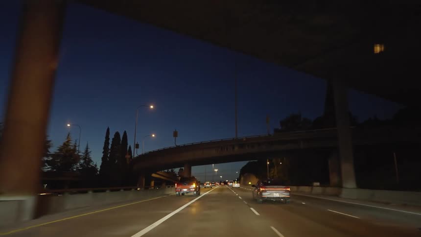 A group of vehicles drive on a highway at night underneath bridges