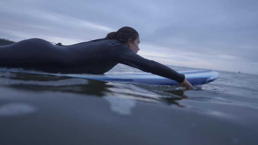 A woman paddles herself laying down on a surfboard