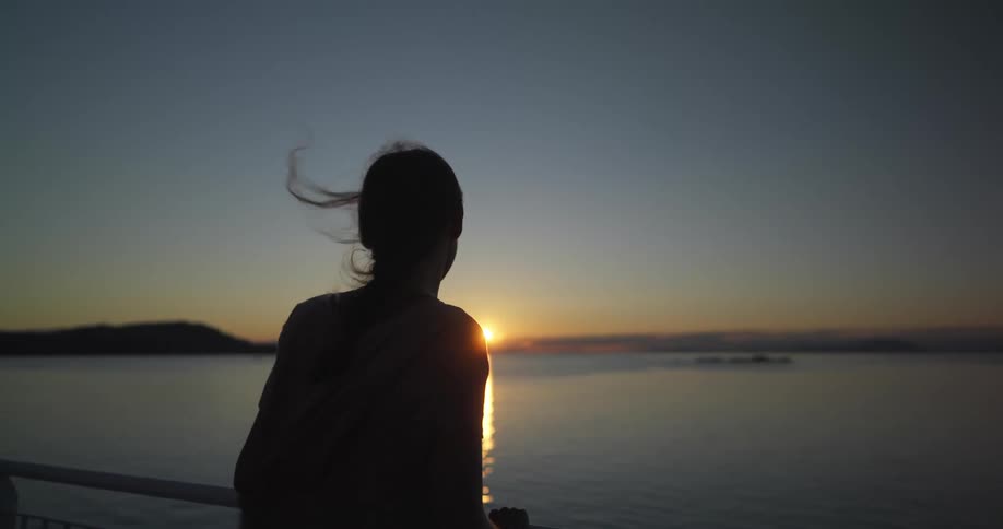 A woman stands on a pier and watches the sun set over the ocean