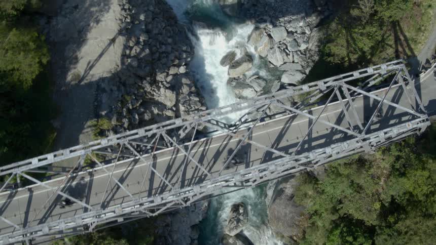 A group of motorcyclists ride across a bridge spanning a ravine
