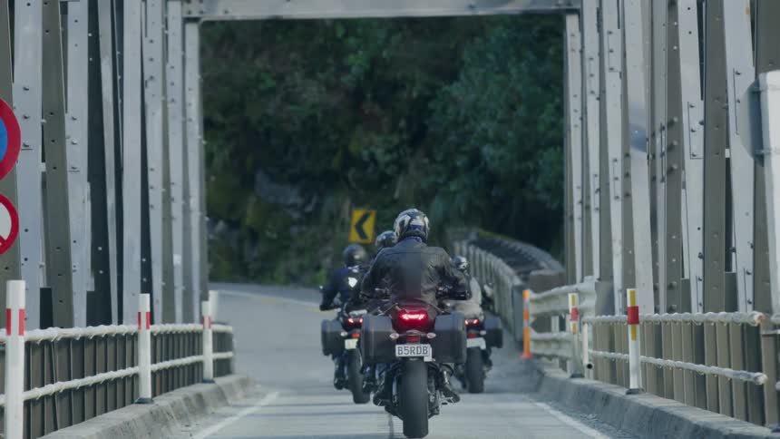 Motorcyclists ride down a narrow bridge