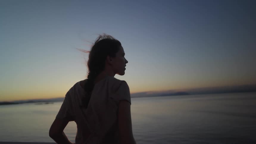 The silhouette of a young woman is seen as she stands overlooking the ocean as the sun sets