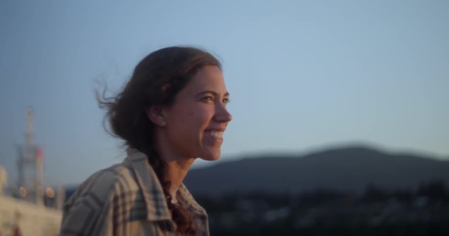 Smiling woman stands with ornate town ornate building and hills in background
