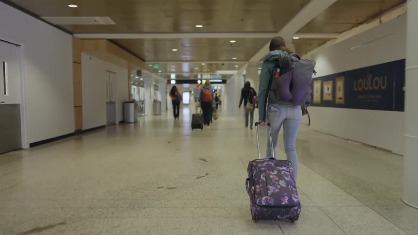 A woman walks through a corridor in an airport while pulling her luggage behind her