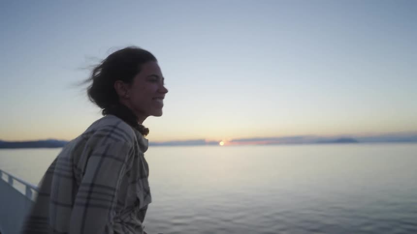 A woman leans over the railing on a pier as the sun sets over the ocean