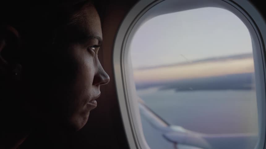 A woman looks out the airplane window over the wing at the water and sunset