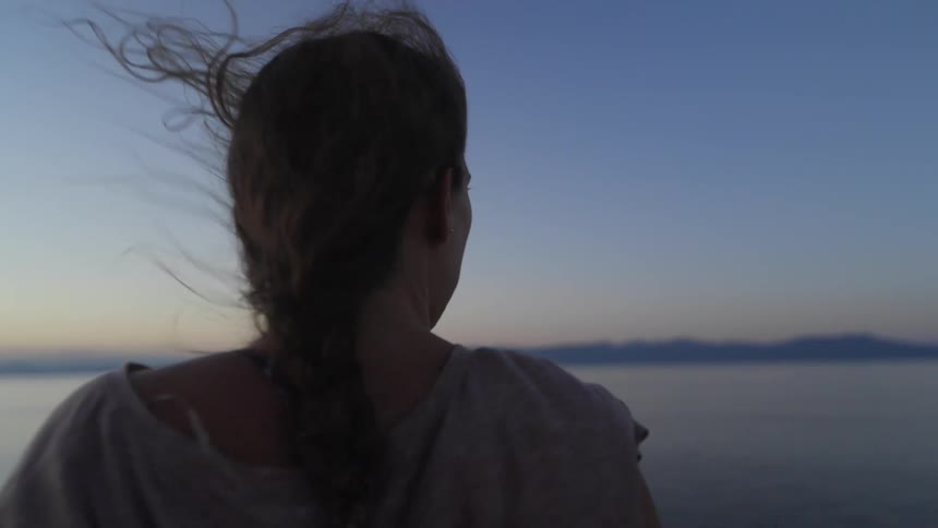 Woman with ponytail and shirt watches sea while traveling by ferry boat at dusk