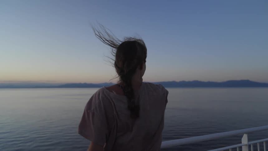 Strong wind blows through a womans hair as she watches the sun set over the ocean